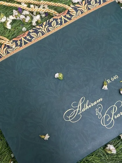 A carry-bag for a deep blue and gold invitation suite, featuring a traditional floral border and sturdy rope handle.