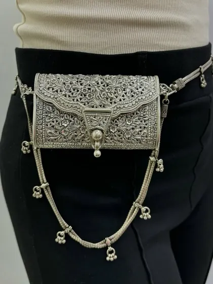A side view of our unique silver waist purse. This angle shows how the intricately carved purse sits elegantly on the hip, attached to a sleek silver belt chain.
