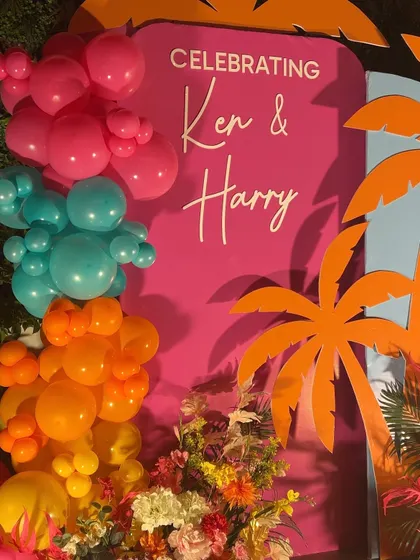 A close-up of the tropical-themed backdrop, showing the bright pink and blue panels with orange palm tree cutouts.
