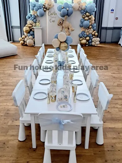 A close-up view of our elegant white table and chair setup for a "Teddy Bear" themed first birthday. The chairs are decorated with delicate blue sashes, showing how easily our classic furniture can be customized.