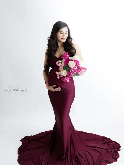 A classic and elegant portrait. The mom-to-be holds a bouquet of flowers, her form-fitting burgundy gown highlighting her beautiful baby bump.