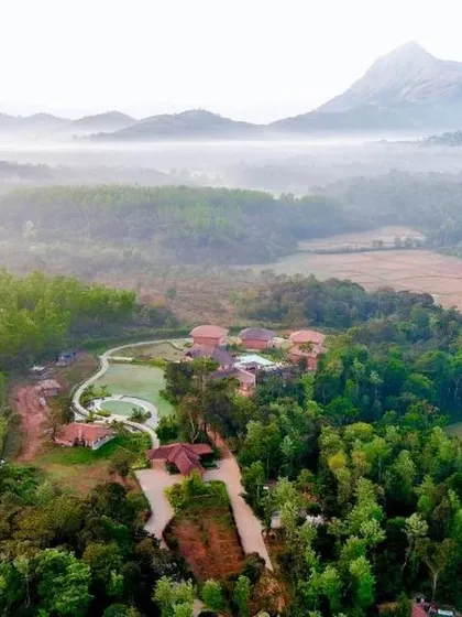 A misty morning at a resort in Sakleshpur, with the property nestled in a valley surrounded by lush forests and mountains.