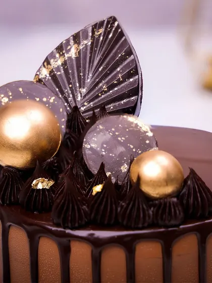 We indulge the senses with this elegant chocolate drip cake. A rich chocolate cake is topped with a fan of decorative chocolate, gold spheres, and delicate gold leaf accents, making it a sophisticated and decadent choice for Father's Day.