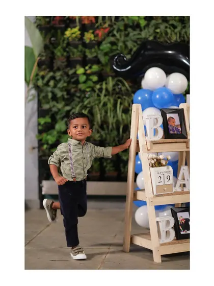 A candid shot of the birthday boy at his 'Little Man' party. The decor in the background includes a personalized prop shelf and a blue and white balloon arrangement.