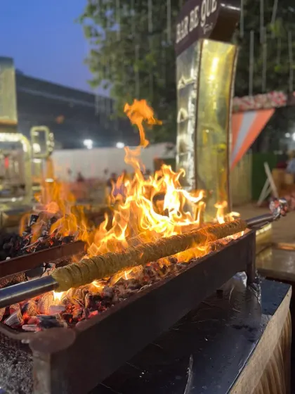 A long seekh kebab cooking over a dramatic open flame, capturing the excitement of live grilling.