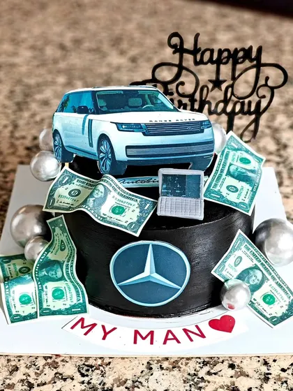 A cake for the man who loves his cars. This design features a Range Rover, a Mercedes logo, and edible money, all on a rich black-frosted cake.