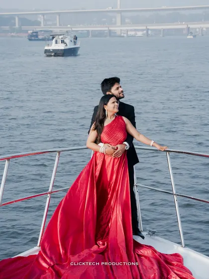 A couple enjoys the view from a yacht, her red gown adding a splash of vibrant color to this serene and romantic pre-wedding scene.