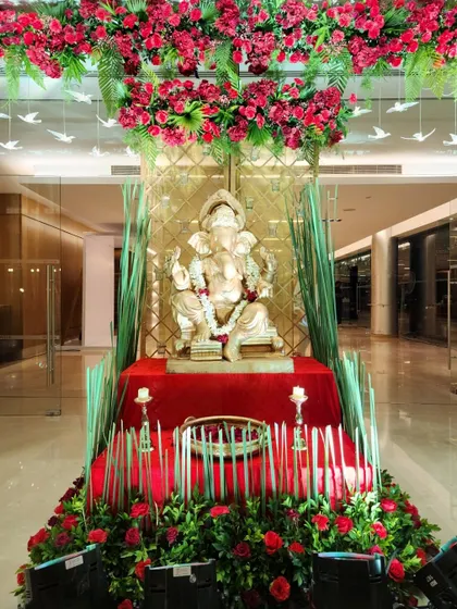 A Ganesha idol placed at the entrance for blessings. The setup is framed by a canopy of red flowers and accented with tall grasses and candles, blending tradition with modern design.
