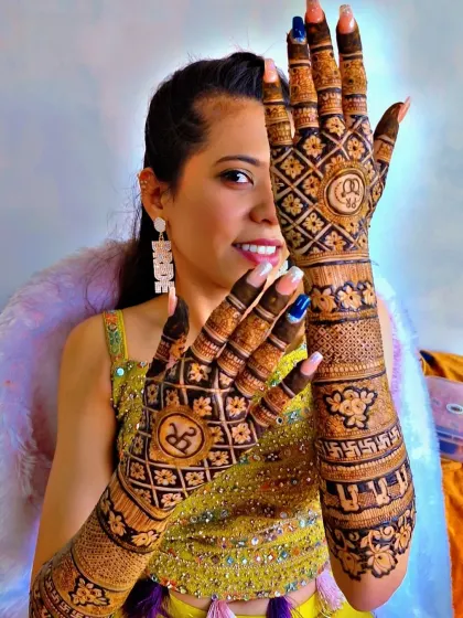 A happy bride-to-be showing off her engagement mehendi. The design features the couple's initials in a unique diamond-shaped frame.