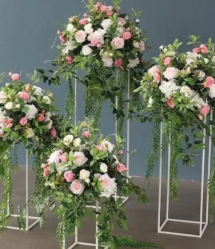 A set of modern floral stands. These white metal frames hold lush arrangements of roses and greenery, perfect for lining a walkway, flanking a stage, or decorating a corporate reception area.