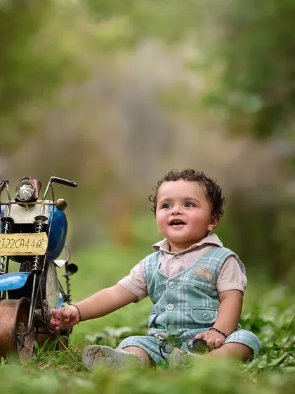 Finding magic in the quiet moments. This toddler is captivated by his toy motorcycle during an outdoor shoot, set against a lush, green natural background.