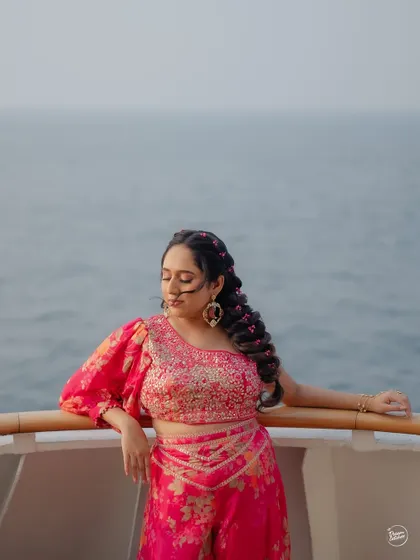 A stunning portrait of the bride in her vibrant pink Haldi outfit, with her braided hair and the ocean behind her.