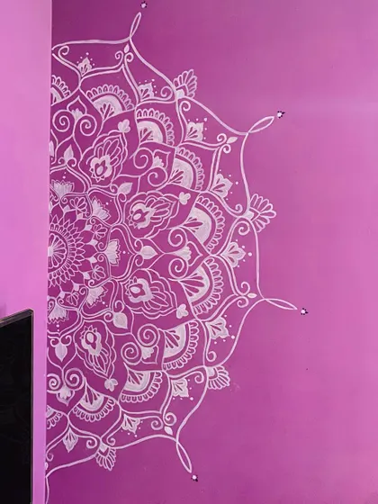 A semi-mandala painted on a vibrant purple wall. The white intricate details stand out, creating a bold and beautiful statement piece in the room.
