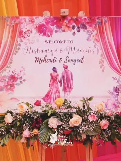 A close-up of the custom illustrated welcome sign for the Mehendi and Sangeet, beautifully decorated with a fresh flower garland.
