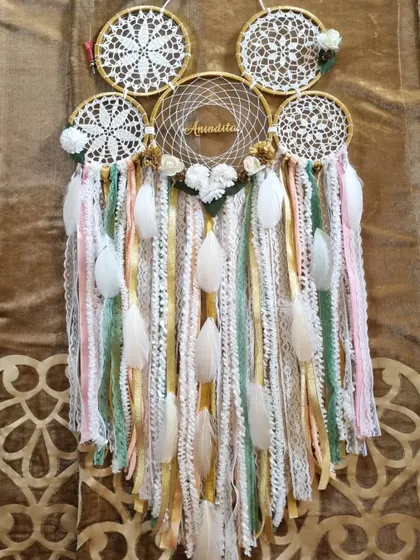 We call this our Gold Dust Dreamcatcher. The mix of gold, green, and pink tones, along with delicate white feathers, creates a warm and elegant piece, personalized for 'Anindita'.