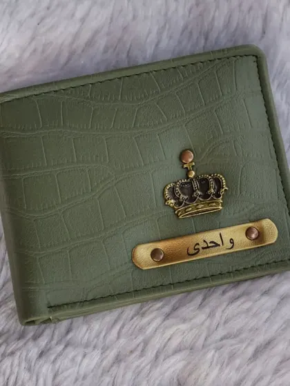 An olive green wallet with a crocodile finish, customized in Arabic script with a crown charm. I can personalize items in different languages, including Hindi and Arabic.
