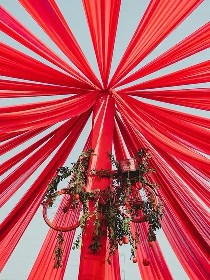 Looking up into the heart of the canopy, the radiating red fabric creates a dramatic and immersive effect, enveloping guests in the theme's core color. A bicycle chandelier adds a touch of rustic whimsy.
