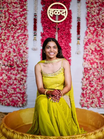 A portrait of the bride sitting in a large golden urn during her Haldi ceremony.