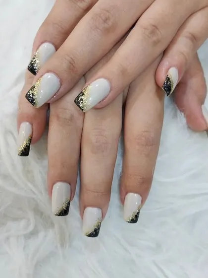 A bold and festive design featuring off-white nails with black and gold glitter tips.