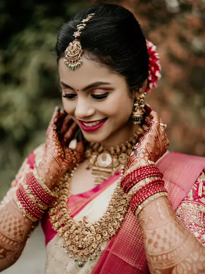 A close-up of a beautiful bride, smiling as she adjusts her traditional gold jewelry.