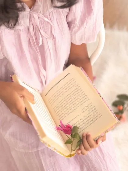 A close-up on the details. A flower tucked inside a book, held by small hands, tells a story of innocence and a love for beautiful things.