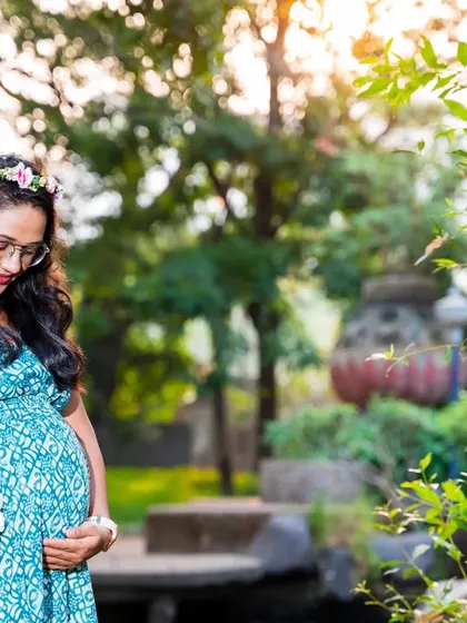 A thoughtful moment in the garden. The mom-to-be, wearing a flower crown, looks down at her bump, holding a basket of fresh flowers.
