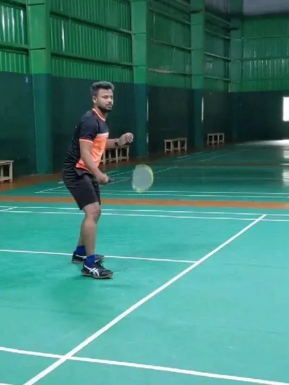 This is the ideal ready position for receiving a serve or a shot. Notice the balanced stance and alert posture, which we emphasize in our adult beginner badminton lessons.