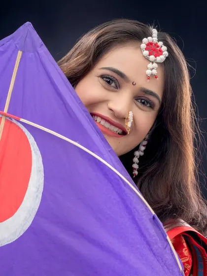 A playful portrait where the woman peeks out from behind a purple kite, or *patang*. This shot captures the fun and festive spirit of the Makarsankranti festival.