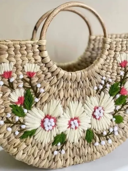 This lovely beach bag, made from woven natural fibers, features delicate white and pink floral embroidery. It's a perfect accessory for a summer outing or a thoughtful, handcrafted gift.