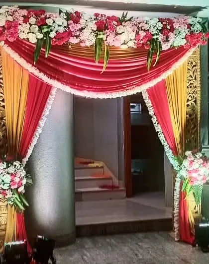 A traditional entrance arch with red and yellow drapes and floral bouquets. The ornate golden frame adds a touch of royalty to the welcome decor.