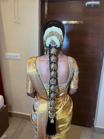 An intricate bridal braid featuring multiple 'Jada Billa' clips with green and pink stone accents, perfectly complementing the bride's golden saree.