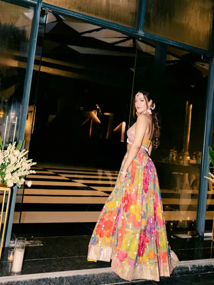 The bride looks back with a smile, her vibrant, multi-colored lehenga in full view, as she makes an entrance at her evening celebration.
