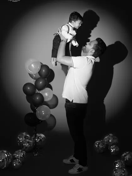 A dramatic black and white photo of a father lifting his son in the air. The spotlight effect creates a powerful and artistic family portrait.