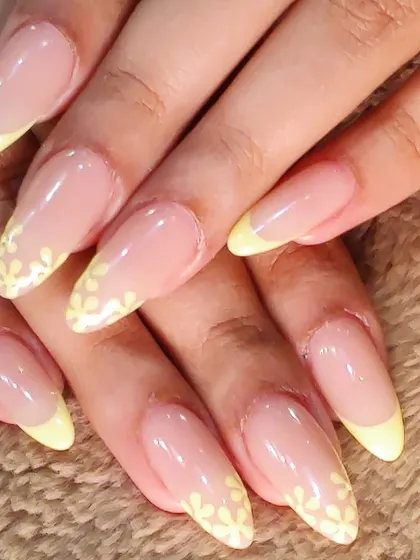 A fresh take on a classic. These elegant, long almond nails feature a delicate pastel yellow French tip, with one nail on each hand adorned with a beautiful, hand-painted white floral design.