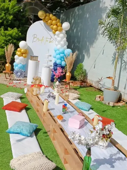 This outdoor bridal shower picnic setup shows a different color variation. The white backdrop is accented with a blue, navy, and gold balloon garland, with a long table ready for a fun celebration.