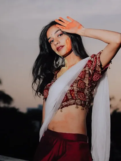 A post-Holi portrait, with the model's hand gently resting on her forehead, showcasing the lingering colors of the celebration against the evening sky.