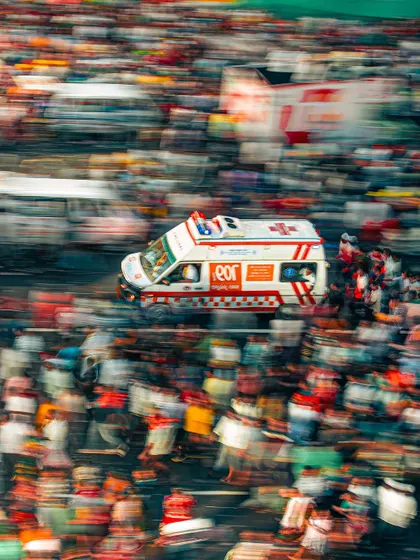 An ambulance with its lights flashing, captured with a slow shutter speed to create a sense of motion amidst the dense crowd of the Rath Yatra.