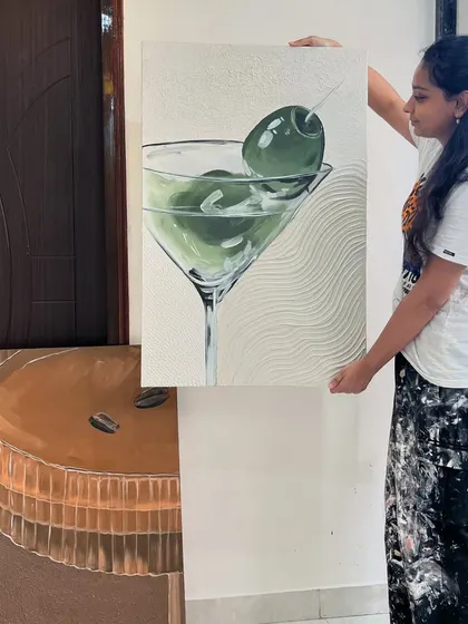 Holding the finished martini painting to show its scale. The textured white background contrasts with the smooth, glossy look of the olives.