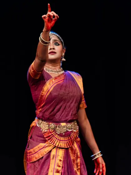 A powerful moment from a solo performance, with the dancer's arm raised in a gesture of command or declaration. The red-painted hands add to the dramatic effect.