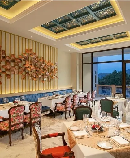 The interior of the IHCL Pilibhit-Haridwar restaurant, where a stunning wall art installation becomes the centerpiece. The design combines a long, comfortable banquette with elegant, custom-upholstered chairs for a luxurious feel.