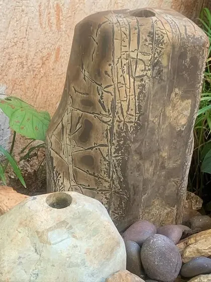 This fountain combines a carved stone pillar with natural rocks and water-loving plants like peace lilies to create a serene corner.