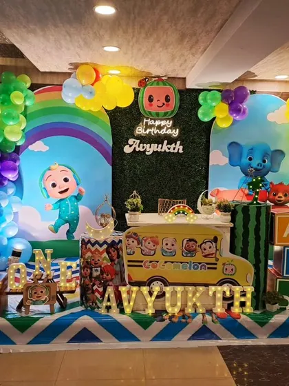We designed this colourful Cocomelon theme for Avyukth's first birthday. The setup includes a greenery wall, character cutouts like the iconic yellow school bus, and themed blocks, all surrounded by a multi-coloured balloon arrangement.