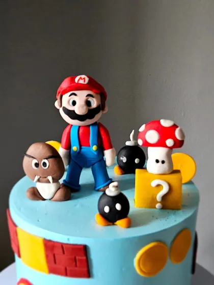 A close-up of the Super Mario cake, showing the incredible detail on the handcrafted Mario figurine and the surrounding game elements like the mushroom and question block.