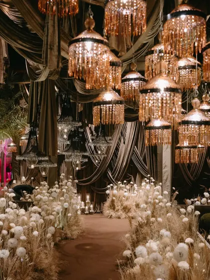 A dramatic Sangeet setup with a canopy of white flowers and shimmering chandeliers, creating a luxurious and opulent environment.