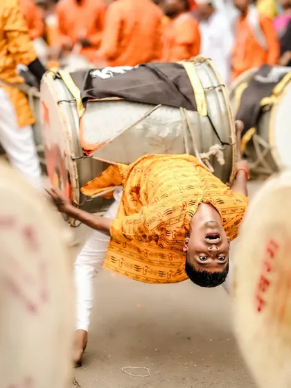 Capturing the peak of energy and devotion. This dynamic shot freezes a dhol player in a moment of acrobatic performance during a street festival, showcasing the raw power and spirit of the celebration.