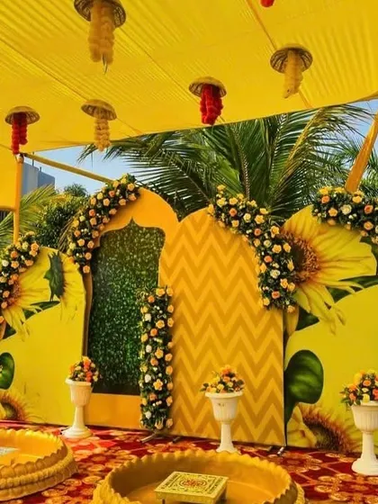 A bright and cheerful Haldi backdrop featuring a sunflower theme. The setup includes large sunflower cutouts, yellow drapes, and fresh floral arches, perfect for a traditional turmeric ceremony.