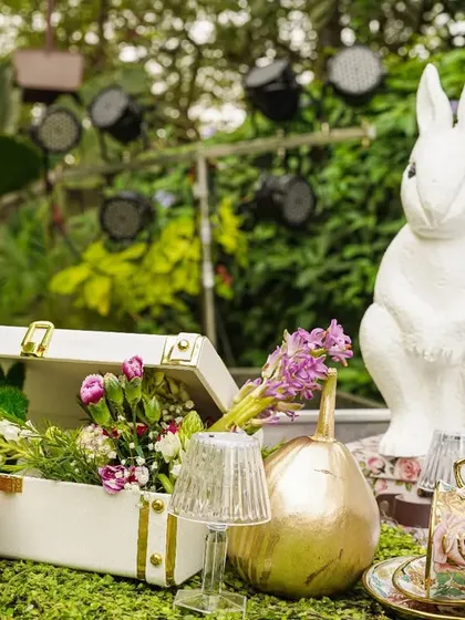 A tabletop vignette featuring a White Rabbit statue, golden gourds, and a vintage suitcase filled with flowers, creating a charming, curated look.