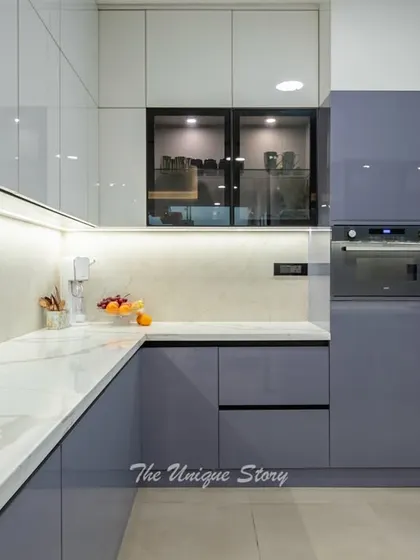 A view of the kitchen's tall units, which house a built-in oven and a large refrigerator. The glossy white finish of the upper cabinets reflects light, making the space feel bright and spacious.
