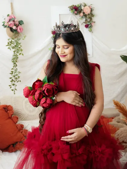 A royal moment for this mama-to-be. Wearing a tiara and a voluminous red gown, she cradles her bump in a cozy, festive setting.
