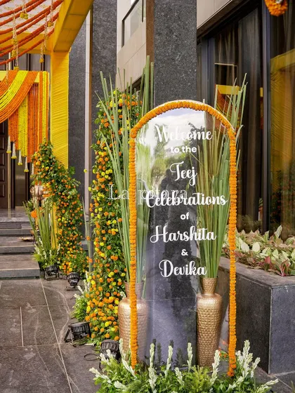 A personalized welcome sign is a detail I love. This clear acrylic sign with elegant calligraphy, framed by marigolds and fresh greenery, warmly greeted guests at the entrance of the Teej celebration.
